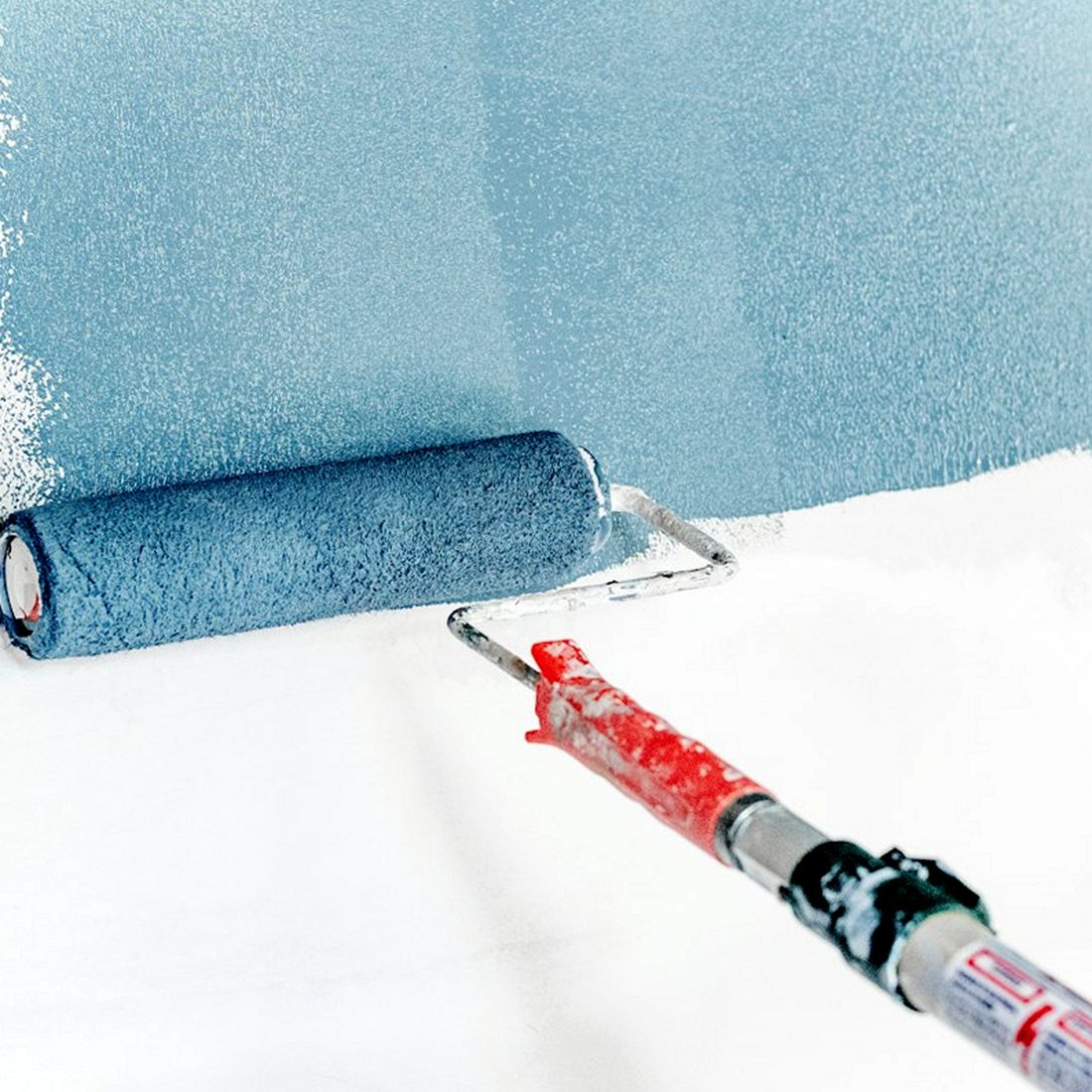 A roller putting blue paint on a white wall